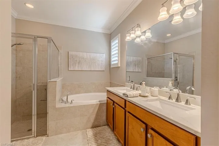 Dual vanity with rectangular sinks, a garden tub, a glass-enclosed shower, wood cabinetry, and a large mirror