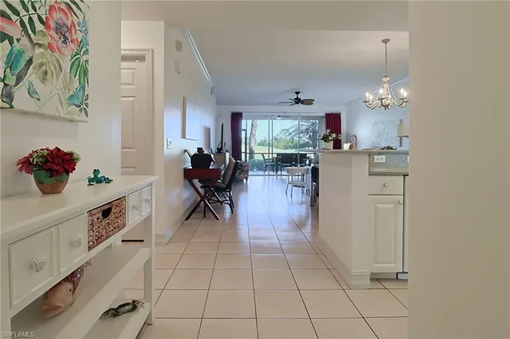 Corridor featuring crown molding, baseboards, light tile patterned floors, and a notable chandelier