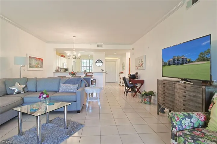 Living room with ornamental molding, a notable chandelier, light tile patterned flooring, and visible vents