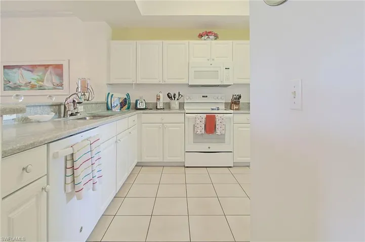 Kitchen with white cabinets, a sink, white appliances, light countertops, and light tile patterned floors