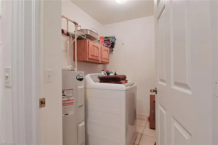 Clothes washing area featuring cabinet space, independent washer and dryer, light tile patterned floors, and electric water heater