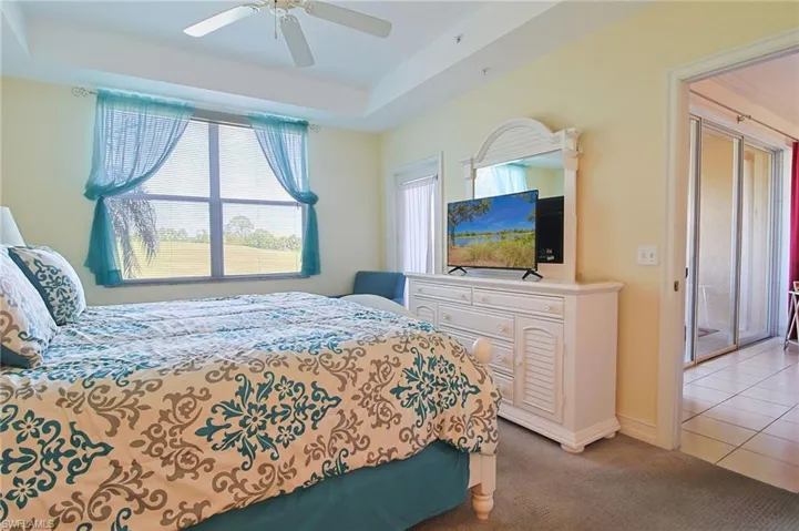 Bedroom featuring ceiling fan, light colored carpet, light tile patterned floors, baseboards, and a tray ceiling