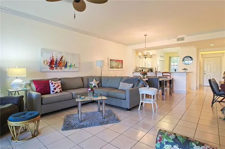 Living room with crown molding, light tile patterned flooring, visible vents, and ceiling fan with notable chandelier