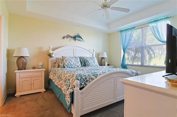 Bedroom with carpet flooring, a raised ceiling, and a ceiling fan