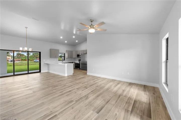 Spacious open-concept living area featuring wood-finish flooring, vaulted ceilings, and recessed lighting