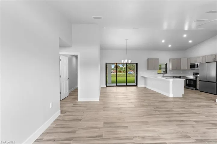 Open-concept interior featuring wood-finish flooring, vaulted ceilings with recessed lighting, and a modern kitchen