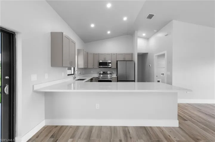 Contemporary kitchen featuring light gray cabinetry, stainless steel appliances, and a spacious white countertop with a breakfast bar