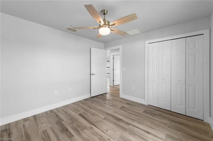 Interior room featuring wood-finish flooring, white baseboards, a ceiling fan with light fixture, and a white bi-fold closet