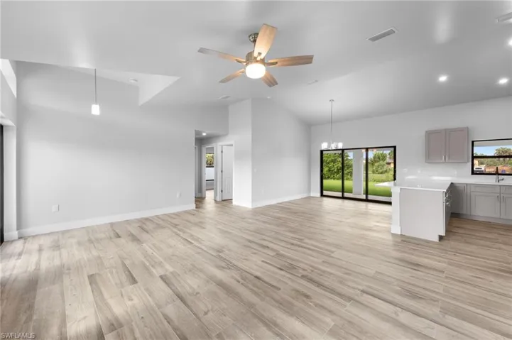 Expansive open-concept living area featuring wood-finish flooring, vaulted ceilings, and recessed lighting