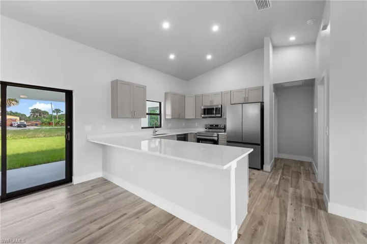Modern kitchen featuring light gray cabinetry, stainless steel appliances, and a white countertop peninsula with bar seating