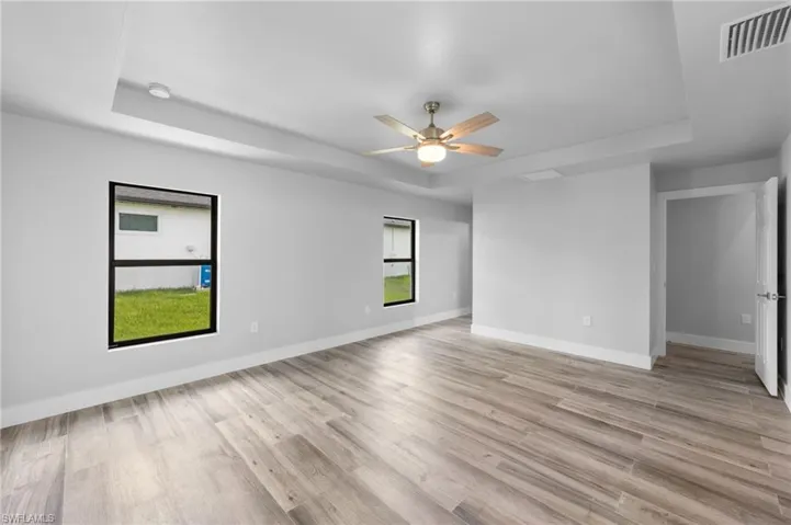 Spacious room featuring wood-finish flooring, a tray ceiling, and a ceiling fan with integrated lighting