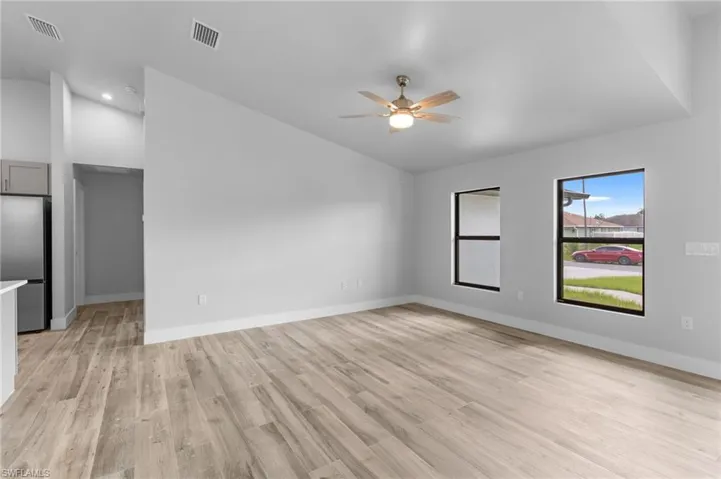 Spacious interior featuring wood-finish flooring, two large windows, a ceiling fan with integrated lighting, recessed lighting, and a partial view of a stainless steel refrigerator