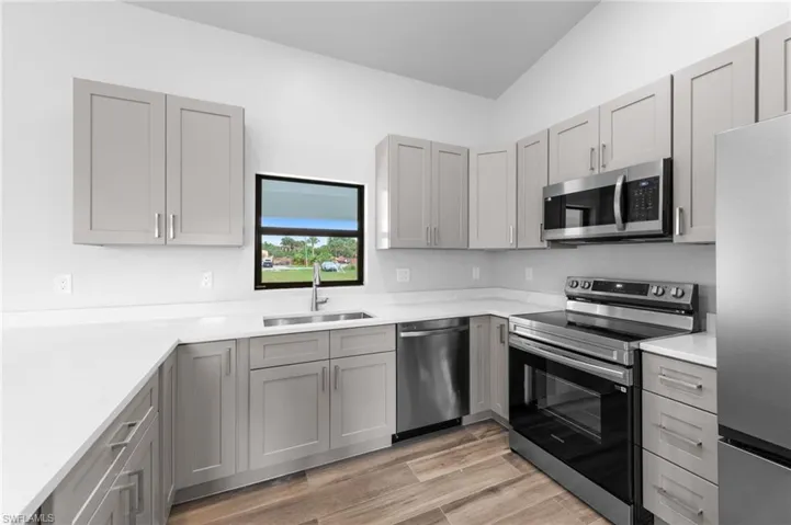 Kitchen featuring light gray cabinetry, white countertops, stainless steel appliances, and wood-finish flooring