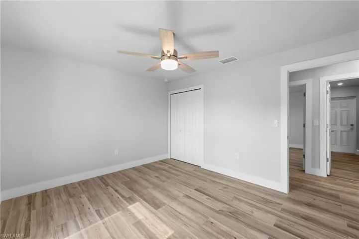 Spacious room featuring wood-finish flooring, light gray wall paint, and a ceiling fan with integrated lighting