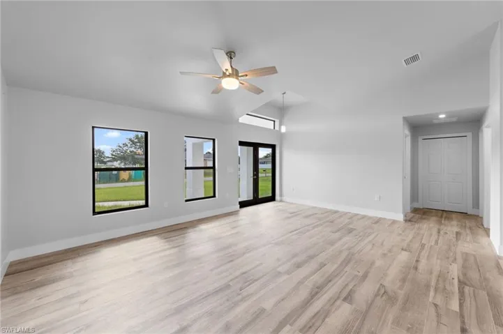 Vaulted ceiling with a contemporary ceiling fan, wood-finish flooring, and black-framed windows