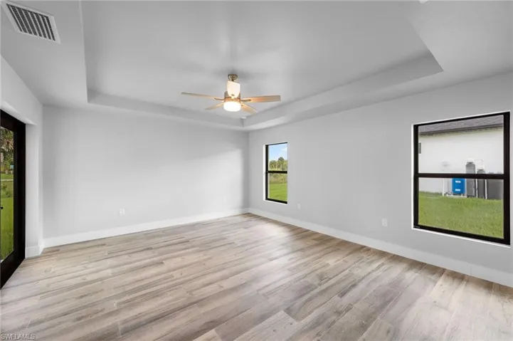 Spacious room featuring wood-finish flooring, a tray ceiling, and a ceiling fan with integrated lighting