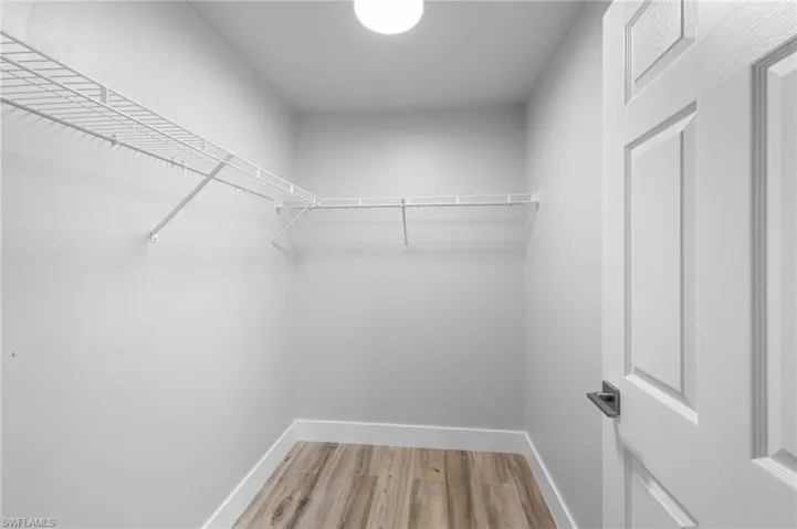Walk-in closet featuring light wood-finish flooring, white wire shelving, white baseboards, and a paneled interior door with matte black hardware