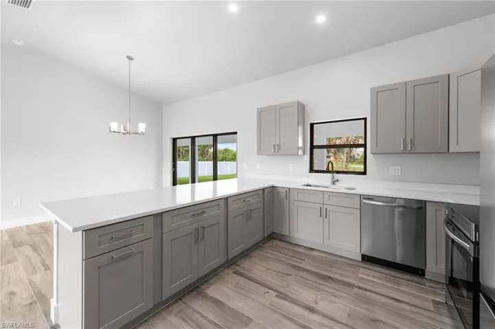 Modern kitchen featuring a large island with white countertops, light gray cabinetry, stainless steel appliances, and wood-finish flooring