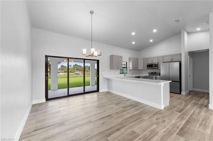 Open-concept living area featuring wood-finish flooring, a contemporary kitchen with stainless steel appliances, pendant lighting, recessed ceiling lights, and sliding glass doors opening to the exterior
