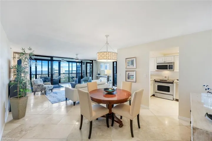 Elegant open-concept living and dining area featuring polished stone flooring, a round wood pedestal dining table with upholstered seating, and a crystal chandelier
