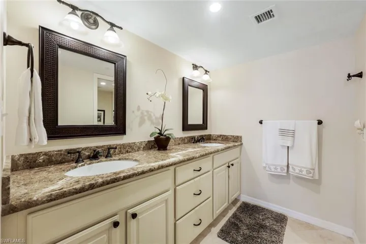 Dual vanity featuring undermount sinks, patterned stone countertops, and cream-colored cabinetry with dark hardware