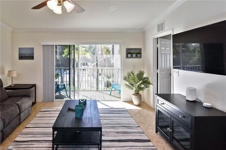Living area featuring a ceiling fan, ornamental molding, and light tile patterned floors