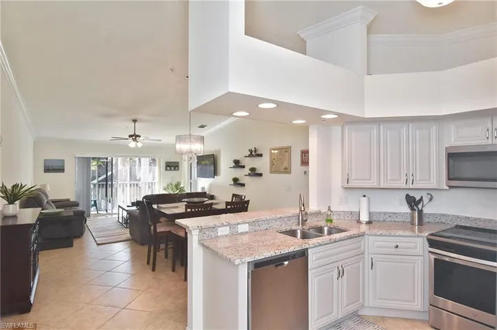 Kitchen with crown molding, stainless steel appliances, a peninsula, light stone counters, and open floor plan