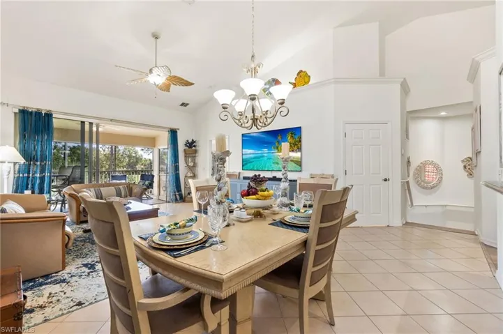 Dining area with a chandelier, light tile patterned floors, ceiling fan, and high vaulted ceiling