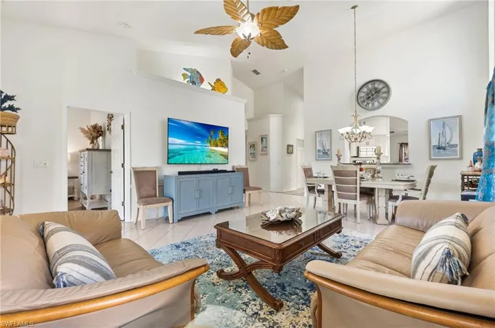 Living area featuring high vaulted ceiling, a ceiling fan, arched walkways, tile patterned flooring, and a chandelier