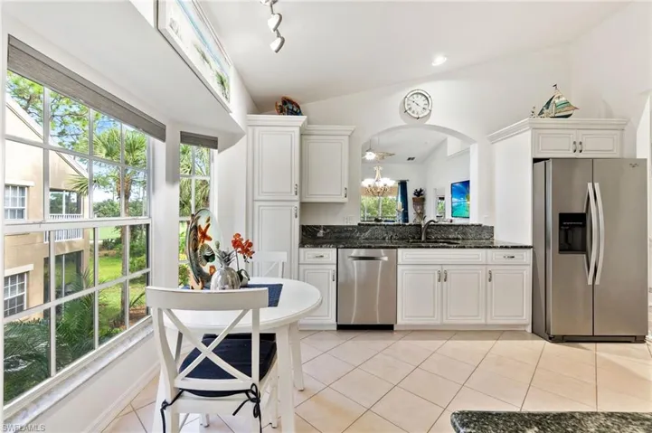 Kitchen with stainless steel appliances, white cabinetry, light tile patterned flooring, dark stone countertops, and lofted ceiling