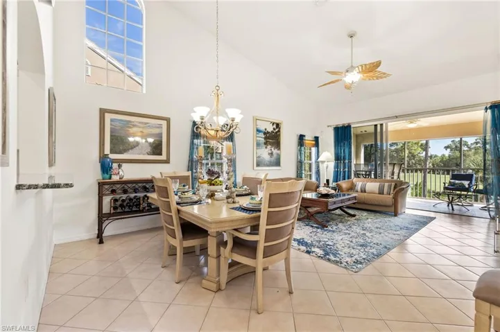 Dining space with high vaulted ceiling, light tile patterned floors, a ceiling fan, and a chandelier