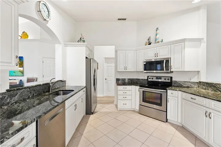 Kitchen featuring stainless steel appliances, dark stone countertops, white cabinetry, light tile patterned flooring, and a high ceiling