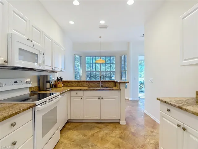 Kitchen featuring white appliances, white cabinetry, decorative light fixtures, and a peninsula