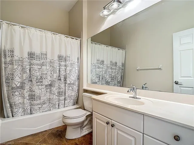 Full bath featuring vanity, shower / bath combination with curtain, and dark tile patterned flooring