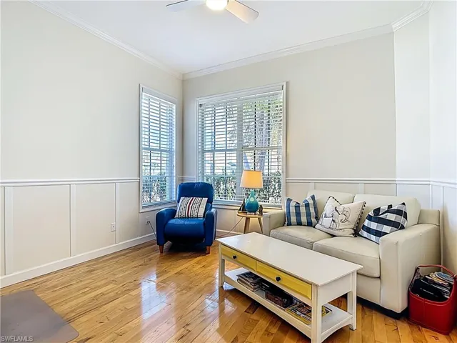 Living area with ornamental molding, light wood-style flooring, a ceiling fan, a decorative wall, and a wainscoted wall