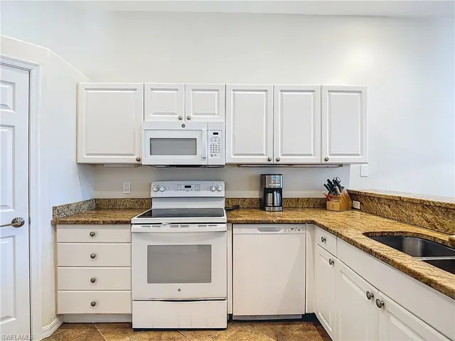 Kitchen featuring white appliances, white cabinetry, and dark stone countertops