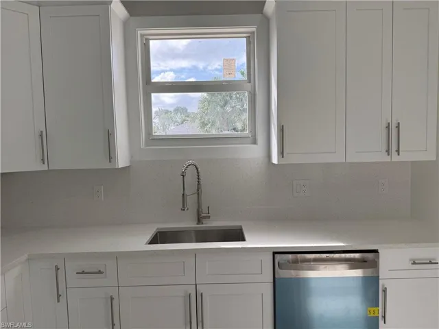Kitchen with stainless steel dishwasher, white cabinets, and light stone countertops