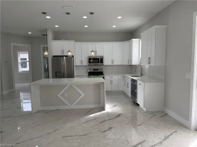 Kitchen with light marble finish flooring, a kitchen island, light stone countertops, appliances with stainless steel finishes, and recessed lighting