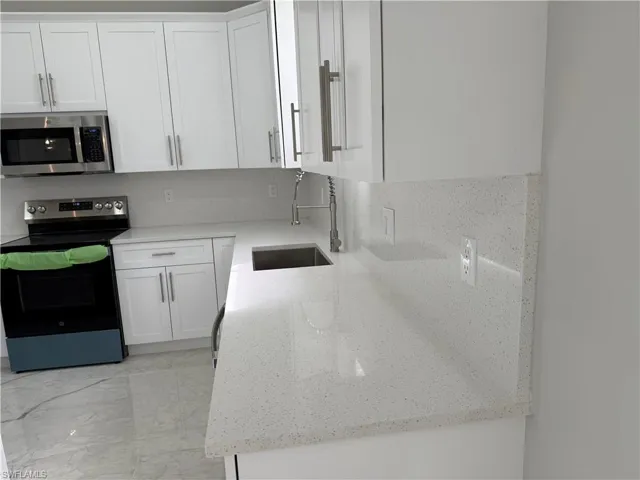 Kitchen with appliances with stainless steel finishes, white cabinets, and light stone countertops