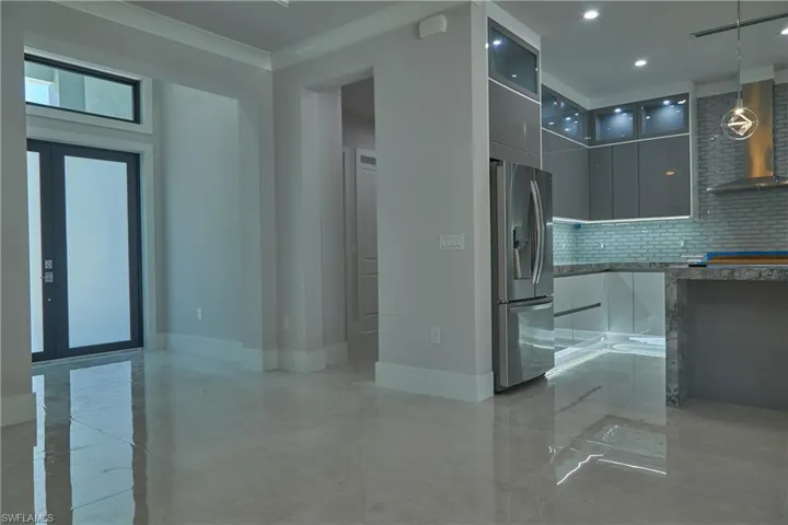 Kitchen with tasteful backsplash, stainless steel refrigerator with ice dispenser, pendant lighting, wall chimney exhaust hood, and light tile patterned floors