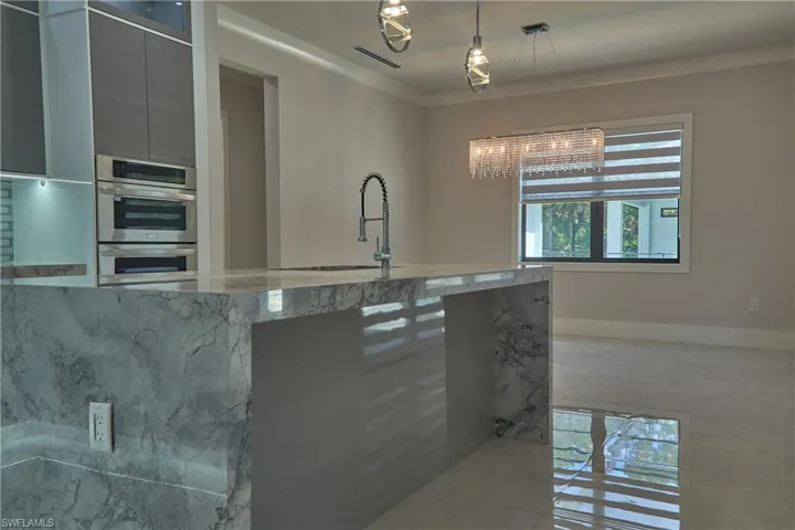 Kitchen featuring pendant lighting, light stone counters, stainless steel double oven, and sink