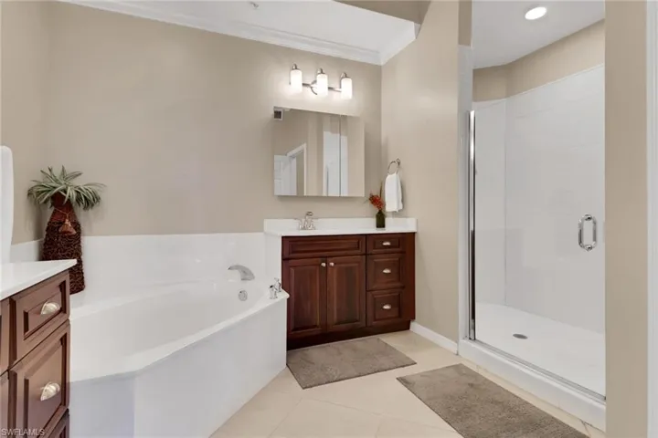 Full bathroom with light tile patterned floors, vanity, a garden tub, a shower stall, and crown molding