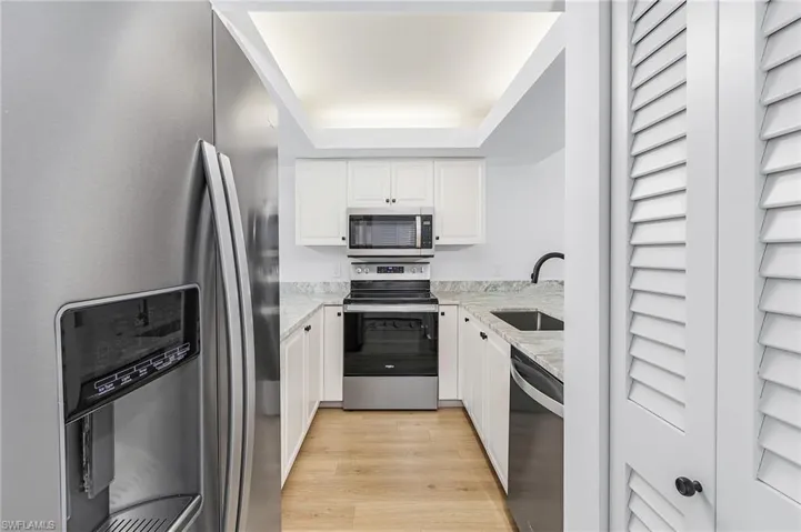 Kitchen featuring white cabinets, sink, a raised ceiling, light hardwood / wood-style floors, and appliances with stainless steel finishes