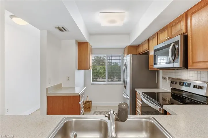 Kitchen featuring appliances with stainless steel finishes, light countertops, light tile patterned flooring, brown cabinets, and tasteful backsplash
