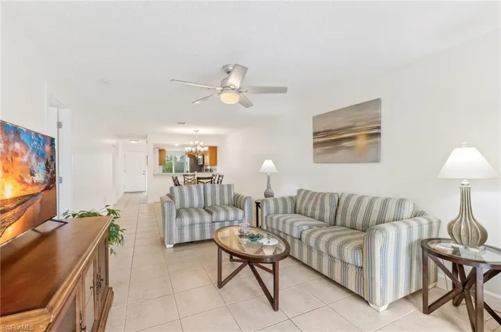 Living area with light tile patterned flooring, a chandelier, a ceiling fan, and a textured ceiling