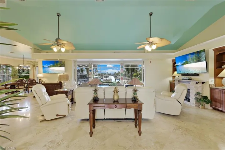 Recessed ceiling with an accent color, two ceiling fans with integrated lighting, tiled flooring, a built-in entertainment center, and pocketing sliding glass doors