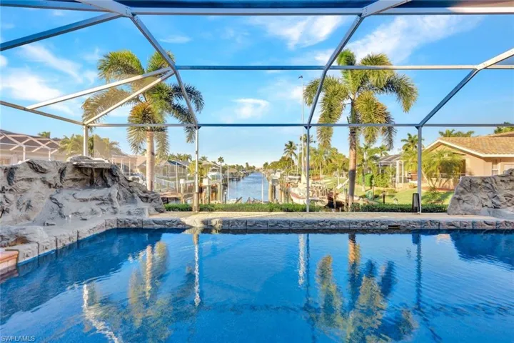 Screened swimming pool and spa featuring rock waterfalls, stone coping, and direct canal access