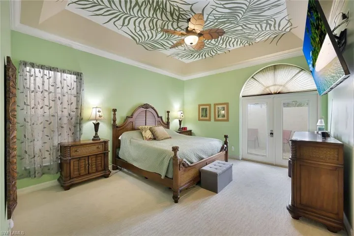Tray ceiling with decorative mural, ceiling fan, arched transom window, and double French doors that lead out to private patio with an above ground spa.