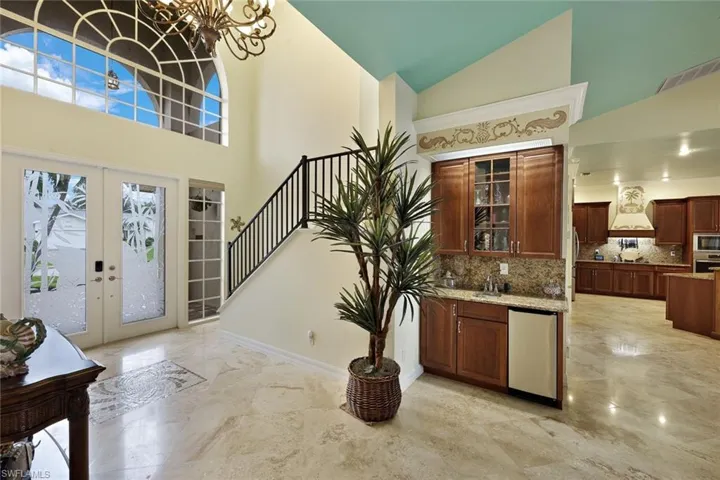 High ceilings with arched transom windows, elegant staircase with wrought iron railing, integrated wet bar with wood-finish cabinetry, and polished stone flooring