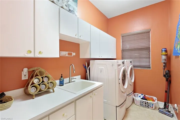Dedicated laundry area featuring a utility sink, extensive white cabinetry, and a bright window
